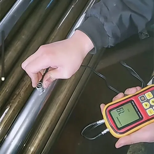 A technician using a digital ultrasonic thickness gauge on a stainless steel tube.